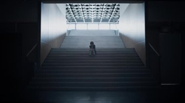 Merdiven boşluğunda tek başına oturan üzgün genç çocuk silueti. Düşünceli, stresli okul çocuğu koridorda poz verirken depresyona giriyor. Koridorda saklanan yalnız genç adam. Okul konseptinde yalnızlık.