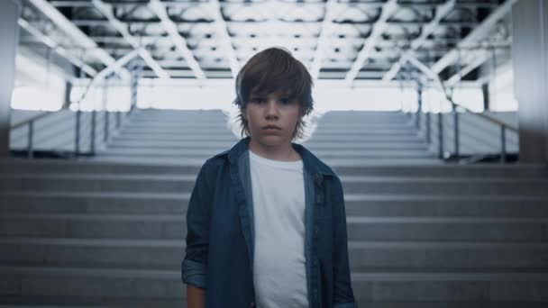 悲しい少年の顔をカメラを見て不幸にも閉じる 空の階段に一人で立って落ち込んでいる少年 授業のいじめの後絶望感が少し動揺します 学校の概念における孤独 — ストック動画