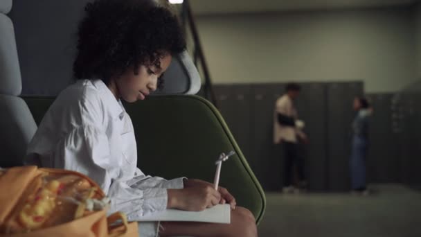 深刻なアフリカ系アメリカ人の10代の学生が学校の休みにスケッチを描く かなり集中した女子高生だけで宿題に集中して座っている ホールで詩を書く思慮深い創造的な巻き毛の女の子 — ストック動画