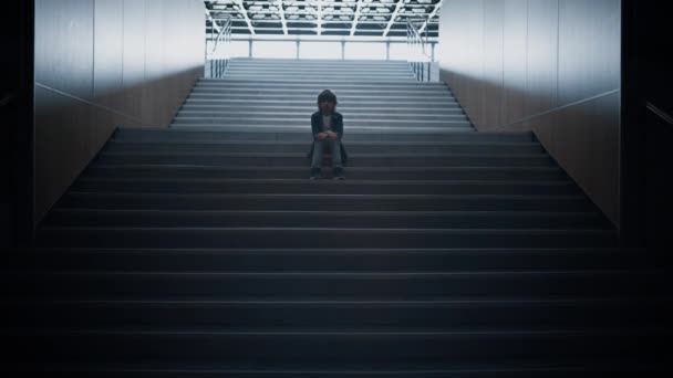 不幸的学童一个人坐在楼梯上 靠得很近 恐惧的恶霸受害者躲藏在空旷的走廊里 感到绝望的学童在未来的学校走廊摆姿势 童年孤独的概念 — 图库视频影像