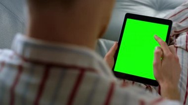 Parmak kaydırma yeşil tablet ekran yakın çekim. Yönetici evdeki uzaktan kumandalı ofiste dijital bilgisayar kullanır. Bilinmeyen adam krom tuşlara dokunuyor. Sosyal medya bağlantılarını kontrol et. Uygulama kullanıcısı kanepede dinlenirken dijital aygıtın keyfini çıkarın.