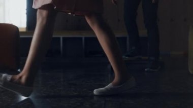 Liseli kız molada okul koridorunda yürüyor. Kapatın. Aktif okul öğrencilerinin önünden geçen, elbise giyen tanınmamış ergen kız öğrenci. Beyaz spor ayakkabılarla yere basan küçük öğrenci bacakları..