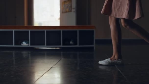 休みの日に女の子の足の学校の廊下を歩いて閉じる キャンパスのタイル張りの床だけで行くスカートを着ている未認識の小学生の女の子 白いスニーカーで廊下を歩く小さな学生の足 — ストック動画