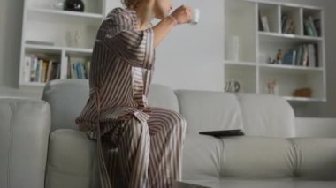 Kadın evde kahve fincanıyla çalışmaya başladı. Samimi, ücra bir yerde tek başına yönetici. Pijamalı, kahve içen, dizüstü bilgisayarını açan güzel, rahat bir bayan. Kanepede oturan güzel kız.