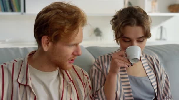 快乐的夫妻在周末小憩片刻喝茶 早上的家庭闲暇时间 快乐的伴侣喜欢喝咖啡 在客厅里在线浏览博客 讨论电影的年轻人 — 图库视频影像