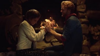 Sevgi dolu bir çift, kır evinde şömineyi ısıtıyor. Sevecen erkek arkadaş, kız arkadaş kış tatilinde el öpüyor. Yakın çekim. Romantik aşıklar kapalı alanda sevgiyi ifade ederler. Rahat rahatlama konsepti