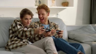 Yarışmacı eş, oturma odasında gülümseyen kızıl kocayla video oyunu oynuyor. Evde joysticklerle mutlu bir aile dinlenmesi. Heyecanlı adam gülümseyen sarışın kız oyun gecesinin tadını çıkarıyor..