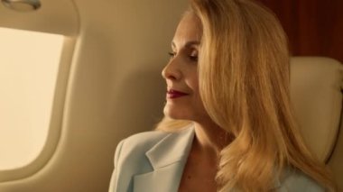 Altın ışıkta uçak penceresine bakan yolcular, yakın plan. Jetle şirket gezisi. Çekici, kendine güvenen iş kadını birinci sınıf lüks içinde rahatlıyor. Zarif zengin kadın takım elbise içinde seyahat etmeyi düşünüyor.