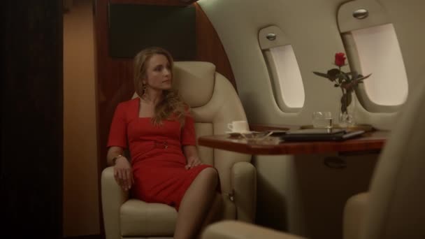 有钱女人一个人坐喷气式飞机迷人的女士穿着红色衣服在舷窗喝咖啡 自信的金发碧眼的女商人想到了在头等舱成功度过的假期 富裕生活方式概念 — 图库视频影像