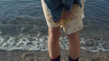Plajda duran şık kız bacakları. Deniz kenarında poz veren, günlük kıyafetlerle tanınmayan bir kadın. Moda botlar giyen hippi bir kadın. Okyanus dalgaları kumlu kıyıya vuruyor. Yaz konsepti 