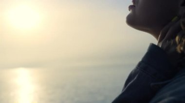 Gün doğumunda plajda rüya gören rahat bir kızın portresi. Deniz ufkunun tadını çıkaran düşünceli bir kadın. Açık havada poz veren kot ceketli bayan hippi. Güneş ışıkları okyanus yüzeyine düşüyor. Gençlik kavramı