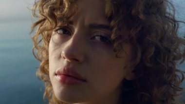 Sahilde kameraya poz veren üzgün kadın. Gözünü kırpan depresif bir kız. Hüzünlü bir kadın. Sakin bayan kameraya bakıyor. Arka planda deniz olan kadın portresi. Hayal kırıklığı konsepti
