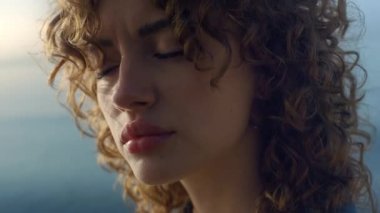 Gün doğumunda sahile bakan hayalperest kızın portresi. Sahil kenarında kameraya poz veren sakin kadın. Bir kadın göz kırpıyor. Doğal makyajlı bir manken yüzü. Yalnızlık kavramı 