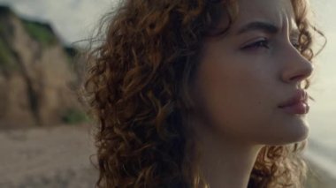 Sahilde güneşin doğuşunu seyreden düşünceli bir kadın. Hayalperest kız başını kameraya çeviriyor. Doğal makyajlı kadın modelin portresi. Dışarıdaki kameraya poz veren genç bayan. Kadın ciddi görünüyor.