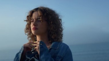 Okyanus sahilinde duran üzgün kız. Üzgün kadın elleriyle boynuna dokunuyor. Kadın hipster depresyonda. Dışarıya bakan üzgün bir bayan. Doğal makyajlı modaya uygun kadın portresi.