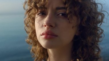 Kameraya bakan üzgün bir kız. Üzgün kadın yüzü portresi. Kadın model dışarıda poz veriyor. Sahilde yürüyen genç bayan. Deniz dalgaları kıyıya vuruyor. Okyanus arka planı. Üzüntü konsepti 