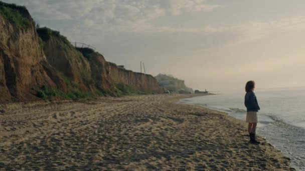 站在海滨的广袤宁静的女人 松懈的女孩在海滩上看日出 女性嬉皮士在海洋度假 日落时走在沙滩上的时髦女士 休闲概念 — 图库视频影像