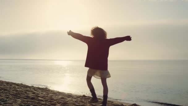 一个积极的女人在海滨举手 情绪化的女孩感到快乐 轮廓模型转过来 日出时分 一位快乐的女士在海滨散步 时尚女人享受自由 胜利的概念 — 图库视频影像