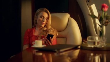 Sarışın kadın, altın güneş ışığında özel uçakla cep telefonuna mesaj atıyor. Endişeli bayan patron astlarına e-posta mesajlarını kontrol ediyor. Sosyal medyada çekici profesyonel akıllı telefon kullanımı iletisi 