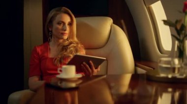 Zarif bir iş kadını tabletle işini bitiriyor. Bardaklar masanın üzerinde. Düşünceli sarışın kadın özel jet uçuşunda tek başına dinleniyor. Başarılı lüks bayan kahve içer. Pazarlıktan sonra rahatlar..