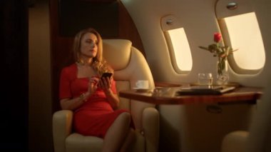 Düşünceli bayan altın güneş ışığıyla uçakta akıllı telefon kullanıyor. Birinci sınıf yolcu istirahatı şirket gezisinde e-posta sosyal medyasını kontrol et. Güzel sarışın iş kadını lüks özel jette alet tutuyor..