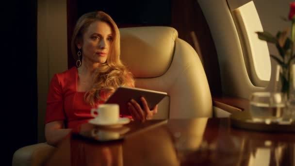 エレガントなビジネスウーマンがタブレットで仕事を終える テーブルの上の開閉パッドガラス プライベートジェット便で一人で休んでいる思慮深いブロンドの女性 交渉の後で成功した高級女性ドリンクコーヒーリラックス — ストック動画