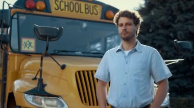 Okul otobüsü şoförünün portresi. Sarı aracın önünde tek başına kameraya bakıyor. Klasik okul servisinde poz veren ciddi profesyonel şoför. Dalgın sakallı adam. Meslek kavramı.