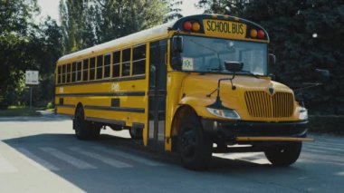 Otoparkta duran boş sarı okul otobüsü güneşli yeşil günün etrafını sardı. Klasik akademik mekiğin dış cephesi. Turuncu okul otobüsü öğrencileri bekliyor. Klasik Amerikan ulaşım konsepti.
