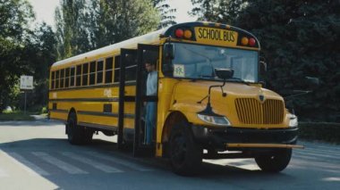Okul otobüsü kulübesinden çıkan genç bir şoför. Boş okul otobüsü otoparkta duruyor. Profesyonel şoför üniforma giyip güneşli bir günde tek başına ekipman kontrol ediyor. Okul çocukları ulaşım konsepti.