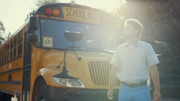 年轻的校车司机独自站在经典的校车旁 严重的专业操作员穿着制服看相机 自信的司机在金色的阳光下摆姿势 专业概念 — 图库视频影像