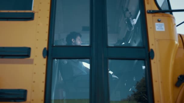 スクールバスのキャビンに一人で座っているプロの男性ドライバー 制服を着た若い運転手が外の景色を見ることができます 真剣な労働者のカメラを開いて車のドアを見る 交通概念 — ストック動画