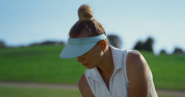 Golf kulübü eğitim kursunda. Spor kadını yakın mesafeden golf topuna vuruyor. Odaklanmış profesyonel golfçü yeşil çimenlikte beyaz üniformalı spor giyer. Tatil eğlencesi konsepti.
