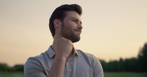 Handsome man celebrate successful golf game on sunset nature fairway course. Portrait of bearded young man enjoying time outdoors activity. Caucasian joyful guy model smiling on field. Leisure concept