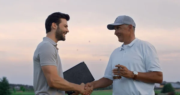 Golf team chatting friendly on sunset golfing field. Two men shake hands outside close up. Handsome club manager group write successful deal on sport activity. Luxury hobby communication concept.