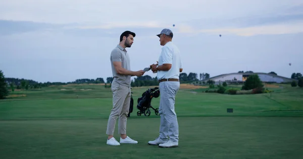 Golf team fight together at green course. Two men argue at country club field. Angry golfers explaining score throw paper on ground. Irritated customer leave go away outside. Partners concept.