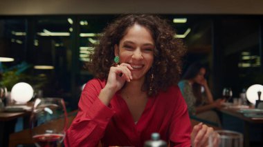 Şık bir restoranda romantik yemek randevusunda kameraya bakan gülen kadın. Çekici Afrikalı Amerikalı kız kafe masasında gülümsüyor. Gece barında güzel elbiseler giyen genç bir bayan. Güzel yemek konsepti.