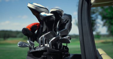 Golf sopası ekipmanları açık hava çantasının içinde. Yeşil golf sahasında golf aletlerini kapatın. Araba çantasına yerleştirilmiş metal golf sopası deri kılıfları. Golf kulübünde aktif bir oyun. Spor konsepti.