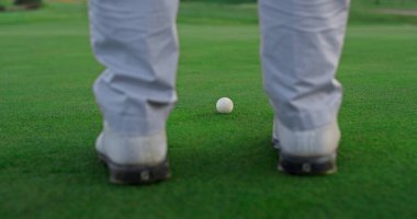 Golf oyuncusu çim yemleme sahasında ayakta duruyor. Dışarıda adam sallama kulübü var. Profesyonel golfçü koç bacakları yaz turnuvasında spor ayakkabı giyer. Zengin yaşam tarzı aktivite kavramı.