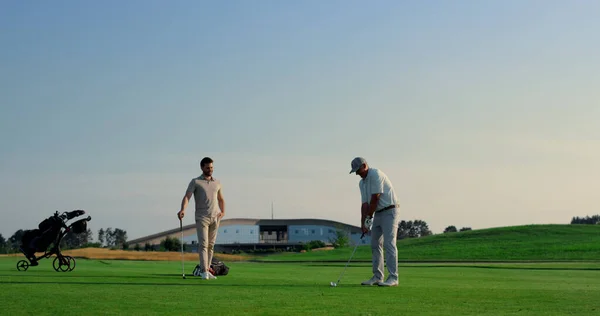 Golf team play sport on green grass field club. Two golfers teeing hitting ball on sunset course. Players group enjoy happy luxury weekend together outdoors. Men having fun on fairway. Active concept.