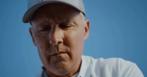 Golfing man face looking distance outdoors. Portrait of old senior wear visor cap sportswear on nature cloudless sky. Professional golf player thinking on sunny summer day. Active retirement concept.