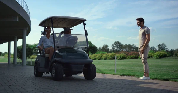 Golf players team meeting at fairway course. Professionals talk sport in cart. Club worker riding golfing car on grass field. Golfers start game on summer sunny morning. Wealthy lifestyle concept.