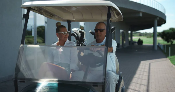 Golf players sit cart get ready outside. Active couple going drive car on course close up. Happy smiling team prepare sport equipment clubs in golfing buggy. Two golfers enjoy summer. Luxury concept.