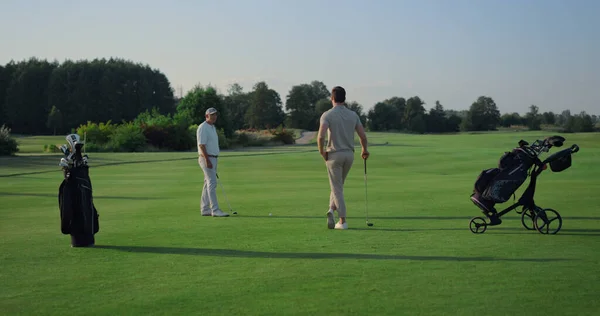 Active men enjoy golf on course field. Two golfers teeing play sport outside. Luxury game players spending time together on holiday weekend resort. Golfing team having fun on fairway. Leisure concept.