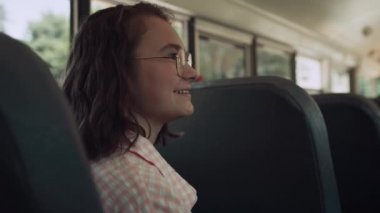 Neşeli gülümseyen genç kız okul otobüsünde arkadaşlarıyla yakın çekim konuşuyor. Sevimli, mutlu, gözlüklü bir öğrenci araç nakliyatında sohbet ediyor. Neşeli liseli kız iletişim kurmaktan zevk alıyor.