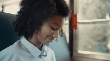 Neşeli kıvırcık saçlı Afrikalı Amerikalı kız aşağıya bakıp otobüste arkadaşıyla konuşuyor. Gülümseyen kıvırcık saçlı esmer öğrenci pencerede tek başına oturuyor. Genç liseli kız, yolcuyla ön tarafta sohbet ediyor. Gençler konsepti.