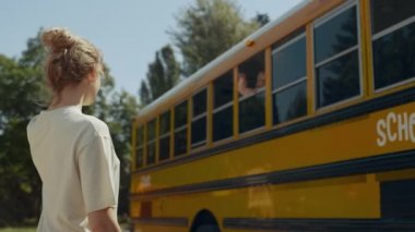 Okul otobüsünün penceresinden annesine el sallayan küçük çocuk. Genç anne, ilkokul çocuğuna hava öpücüğü yolluyor. Gülümseyen şirin çocuk güneşli bir sabah için sınıftan ayrılıyor..