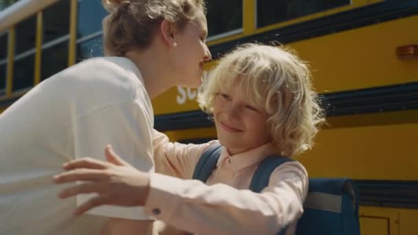 妈妈和小儿子在校车上拥抱的快乐 笑男孩看相机近身 卷曲快乐的小学生下课后去看妈妈 在学术穿梭机旁愉快的问候 — 图库视频影像