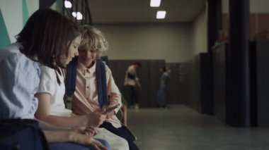 Okul koridorunda tablet bilgisayar izleyen neşeli sınıf arkadaşları. Şirin heyecanlı öğrenciler tatilde bloknotlarıyla internette sohbet ediyorlar. Gülümseyen öğrenciler koridorda oturmuş internet sörfünün keyfini çıkarıyorlar. Teknoloji konsepti.