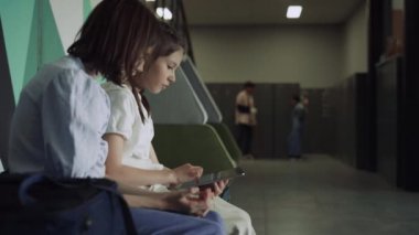 Okul tatilinde internet tableti kullanarak gülümseyen liseli kızlar. İki genç okul arkadaşı dolapların önünde konuşuyor. Neşeli ergenlik çağındaki çocuklar oyun oynamaktan zevk alıyor. Eğitimde teknoloji