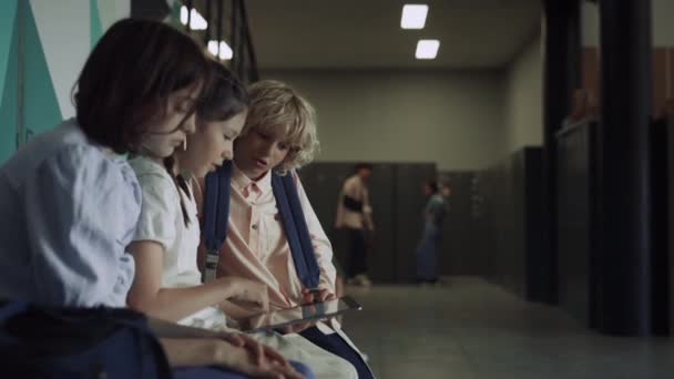 三个专注的学生坐在学校大厅里用平板电脑 认真有兴趣的朋友一起在网上玩触摸屏 在走廊里拿着数字小玩意的十几岁以下儿童 — 图库视频影像